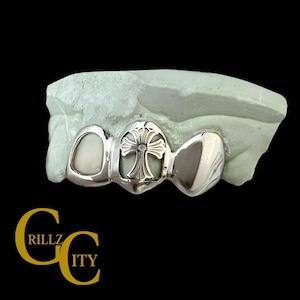 May include: Silver-colored grill with a cross design in the center, set on a light green mold. The grill has a polished finish and is designed to fit over teeth. The logo "RILLZ CITY" is in the bottom left corner.