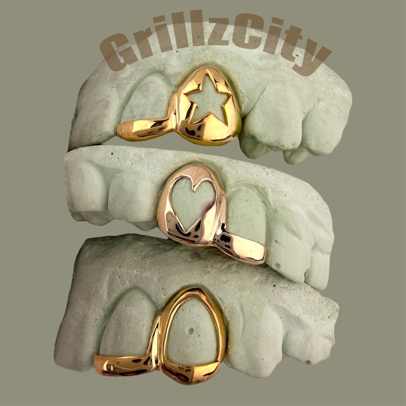May include: Gold-colored grillz with star, heart, and oval designs are displayed on dental molds. The text "GrillzCity" is visible at the top. The grillz are shown in a stacked arrangement, showcasing the variety of styles.
