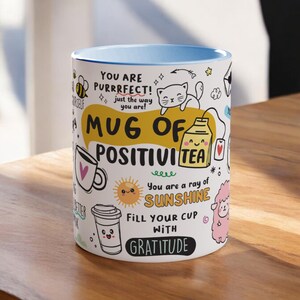 May include: White ceramic mug with a blue rim. The mug features a colourful design with the text "Mug of Positivi Tea" and other positive messages.
