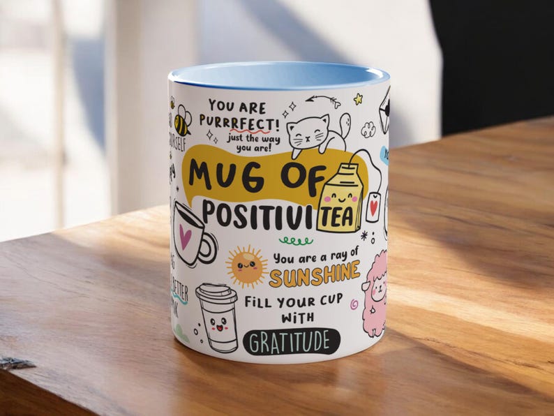 May include: White ceramic mug with a blue rim. The mug features a colourful design with the text "Mug of Positivi Tea" and other positive messages.