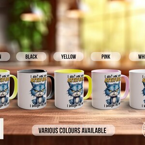 May include: Five ceramic mugs with a yellow, black, green, pink, and white rim. Each mug features a cartoon cat with a grumpy expression and the text "I don't need your attitude I brought my own".