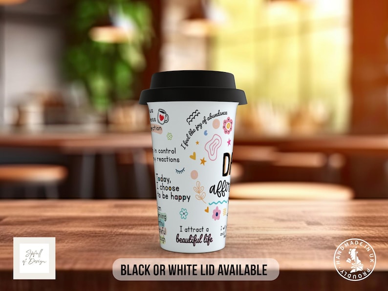 May include: White travel mug with a black lid. The mug has colorful illustrations and text that reads "I feel the joy of abundance", "in control of my reactions", "Today, I choose to be happy", "I attract a beautiful life", and "Daily affirmations".