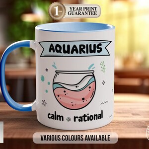Könnte beinhalten: Weißer Keramikbecher mit blauem Griff und Innenrand. Der Becher zeigt das Wort "AQUARIUS" über einer Fischglas-Illustration, mit den Wörtern "ruhig" und "rational" darunter. Der Text "VARIOUS COLOURS AVAILABLE" ist ebenfalls vorhanden.