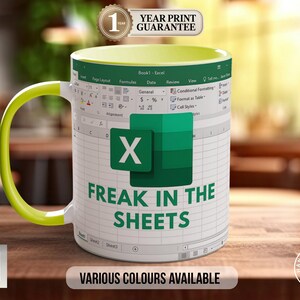 Könnte beinhalten: Weiße Keramik-Tasse mit grünem Innenraum und Griff. Die Tasse zeigt ein Excel-Tabellen-Design mit dem Text "FREAK IN THE SHEETS" in Grün. Außerdem gibt es einen Aufkleber "1 YEAR PRINT GUARANTEE".