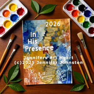 May include: An art print titled "In His Presence" with the year 2026. The artwork features a collage of sheet music and watercolour paint in shades of blue, yellow, and brown. Paintbrushes and paint palettes surround the print.
