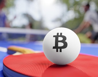 Può includere: Una pallina da ping pong bianca con un simbolo Bitcoin nero su di essa, appoggiata su una racchetta da ping pong rossa e blu.