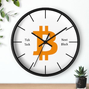 May include: A round wall clock with a black frame and a white face. The clock features an orange Bitcoin symbol in the center, with the words "Tick Tock" and "Next Block" on the face.