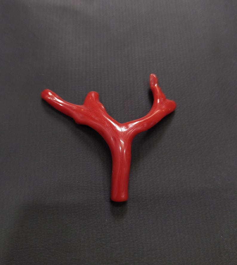 May include: A bright red coral branch with a natural, organic shape. The coral has a smooth, polished finish and a branching structure. The image is set against a dark background, accentuating the coral's colour and texture. This piece could be used for jewellery or decorative purposes.