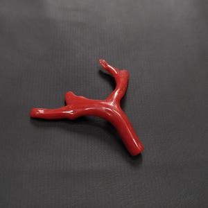 May include: A bright red coral branch with a natural, organic shape. The coral has a smooth, polished finish and a branching structure. The image is set against a dark background, emphasizing the coral's colour and texture.
