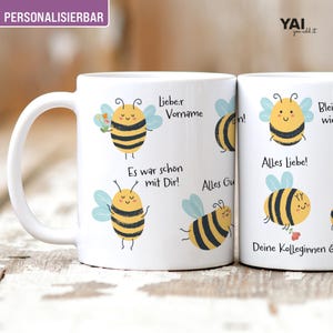 Pode incluir: Caneca de cerâmica branca com abelhas de desenho animado com listras pretas e amarelas, asas azuis e rostos sorridentes. A caneca tem texto em alemão, incluindo "Liebe:r Vorname" e "Alles Liebe!" A caneca é personalizada.