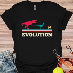 May include: Black t-shirt with a graphic of a dinosaur, a velociraptor, and a chihuahua, with the word "EVOLUTION" printed below the images.