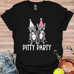 Pode incluir: Camiseta preta com um gráfico branco de dois cães pit bull usando chapéus de festa. O texto "Pitty Party" é impresso abaixo dos cães.