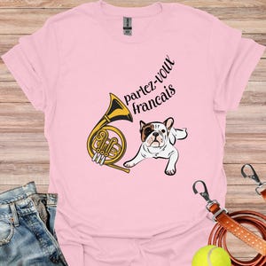 May include: Pink t-shirt with a French bulldog and a French horn. The text on the shirt says "parlez-vous francais".