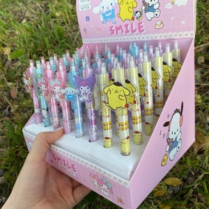 May include: A pink and white display box filled with 48 colorful pens featuring cartoon characters. The pens have clear barrels with colorful ink and character toppers. The box has the word "SMILE" printed on it.