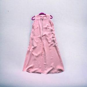 May include: A sleeveless, pale pink dress with a silver zipper down the front, hanging on a purple hanger. The dress has a simple, elegant design and appears to be made of a smooth, flowing fabric.