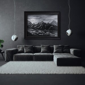 Puede incluir: Una pintura en blanco y negro de una cordillera con un cielo oscuro y nublado. La pintura está enmarcada en un marco negro y cuelga de una pared oscura sobre un sofá negro.