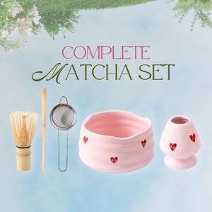 May include: A complete matcha set includes a bamboo whisk, a sifter, a pink ceramic bowl and a pink ceramic matcha holder. The bowl and holder are decorated with red hearts. The text "COMPLETE MATCHA SET" is displayed.
