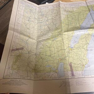 May include: Folded vintage map of Green Bay, Wisconsin, featuring detailed road networks, water bodies, and geographical features. The map is printed in shades of green, yellow, and blue, with a faded appearance, suggesting age. The map is folded.