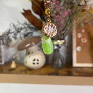 May include: A gold chain charm with a green glass jar and a mini pie with white icing.