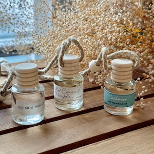 Può includere: Tre piccole bottiglie di vetro con tappi di legno ed etichette, sospese da una corda. Le etichette recitano "Oat Meal Milk &", "Salted Caramel Pumpkin" e "Cashmere by NEESH&CO". Le bottiglie sono su una superficie di legno, con fiori secchi sullo sfondo.
