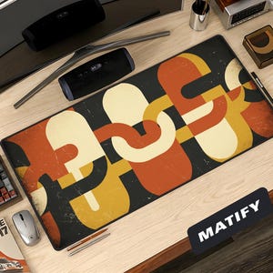 May include: A rectangular desk mat with a retro geometric design in orange, cream, and yellow on a black background. The mat is on a light wood desk with a keyboard, mouse, and other office accessories. The word "MATIFY" is printed on the mat.
