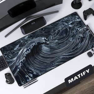 Op de afbeelding: Een grote zwart-witte bureaumat met een golfontwerp, met het woord "MATIFY" in het wit. De mat is omgeven door een gebogen monitor, luidspreker, microfoon, toetsenbord, muis en andere technische accessoires.
