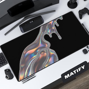 Puede incluir: Alfombrilla de escritorio rectangular negra con un diseño grande, iridiscente y líquido. La alfombrilla está rodeada de accesorios informáticos, como un teclado, un ratón, un monitor, un micrófono y un mando de juegos. La alfombrilla tiene la palabra "MATIFY" impresa.