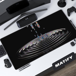 Könnte beinhalten: Schwarze rechteckige Schreibtischunterlage mit einem farbenfrohen, wirbelnden Design. Die Matte hat ein zentrales Muster aus konzentrischen Kreisen mit einem Spritzeffekt. Das Wort "MATIFY" ist weiß auf einem schwarzen Rechteck unten rechts gedruckt.