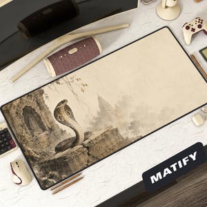 Puede incluir: Alfombrilla de ratón rectangular con borde negro. Presenta una ilustración detallada de una cobra frente a un templo antiguo. El fondo es de color beige descolorido. La palabra "MATIFY" está impresa en blanco sobre un rectángulo negro.