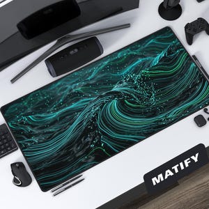 Puede incluir: Una alfombrilla de escritorio grande, negra y verde, con un diseño de olas fluidas. La alfombrilla está rodeada de accesorios informáticos, como un monitor, un teclado, un ratón y un mando de juegos. La alfombrilla tiene la palabra "MATIFY" en texto blanco.