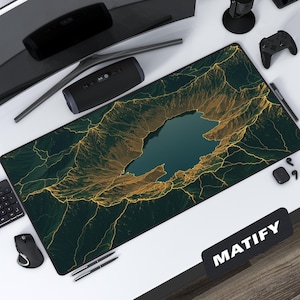 May include: A large rectangular desk mat featuring a detailed landscape design with a central lake. The mat has a dark green and gold color scheme, with the word "MATIFY" in white on a black rectangle in the lower right corner.