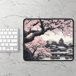 Op de afbeelding: Een rechthoekige muismat met een zwart-witte illustratie van een Japans landschap met een grote kersenbloesemboom op de voorgrond, een traditioneel gebouw bij een vijver en een bergtop op de achtergrond met roze bloemen.