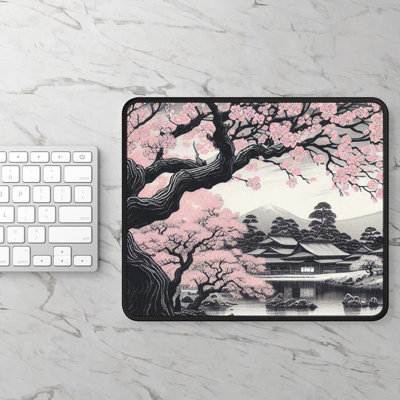 Op de afbeelding: Een rechthoekige muismat met een zwart-witte illustratie van een Japans landschap met een grote kersenbloesemboom op de voorgrond, een traditioneel gebouw bij een vijver en een bergtop op de achtergrond met roze bloemen.