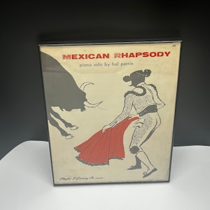 May include: Framed vintage print titled "Mexican Rhapsody" featuring a matador with a red cape facing a bull. The artwork is in black, red, and beige tones, with text at the top and bottom of the print.