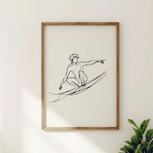 May include: A black and white line drawing of a person surfing on a wave. The drawing is framed in a light wood frame and is hanging on a white wall.