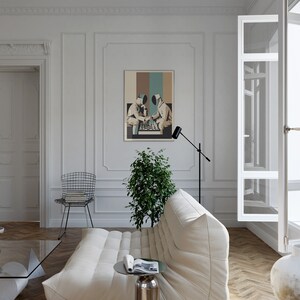 May include: A white couch with a black floor lamp and a framed poster of two figures playing chess. The poster has a colorful abstract background.