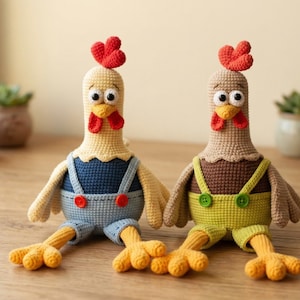 May include: Two handmade crochet chicken dolls. One chicken is yellow with blue overalls, and the other is brown with green overalls. Both have red combs, yellow feet, and large googly eyes. The dolls are sitting on a wooden surface.