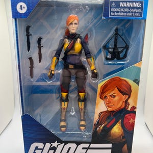 May include: A G.I. Joe Classified Series Scarlett action figure in a clear plastic package. The figure is wearing a yellow and blue uniform with a red-haired head. The package includes a crossbow and three knives. The box has the text "G.I. Joe Classified Series Scarlett".