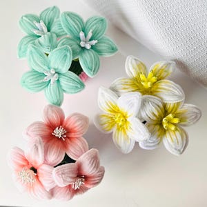 May include: Four sets of flower hair accessories in various colors. The sets include mint green, white with yellow centers, and pink flowers. Each flower has a white center. The accessories are likely made of fabric.