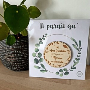 May include: A white card with green floral designs and gold lettering reads "Il parait qu'" and "Une Amie formidable fait toujours une Marraine exceptionnelle".
