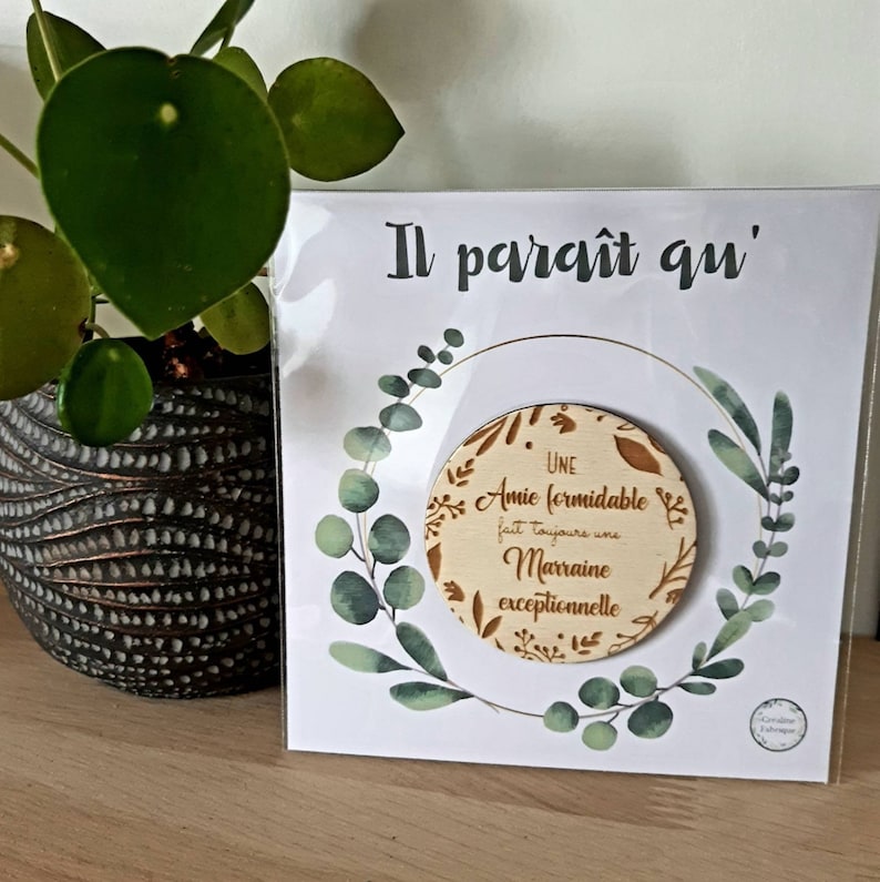 May include: A white card with green floral designs and gold lettering reads "Il parait qu'" and "Une Amie formidable fait toujours une Marraine exceptionnelle".
