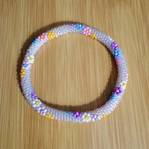 May include: A beaded bracelet with a floral design. The bracelet is made of clear beads with small, colorful flower accents in pink, yellow, purple, and blue. The bracelet is approximately 2.5 inches in diameter.