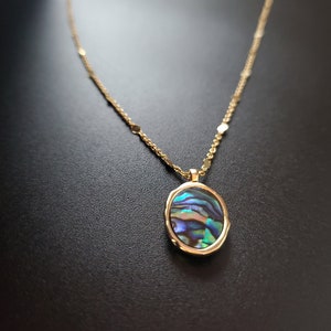 May include: A gold chain necklace with a round pendant featuring a blue, green, and purple abalone shell.