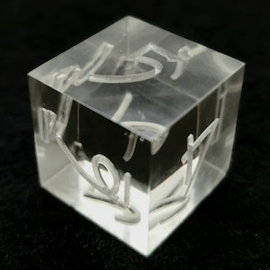 May include: A clear acrylic cube with the numbers 1 through 6 etched on each side. The numbers are visible through the cube.