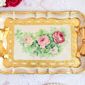 Peut inclure: Un plateau décoratif rectangulaire avec une base crème et une bordure dorée. Le plateau présente un motif floral de roses roses et rouges avec des feuilles vertes. Des poignées dorées en forme de nœud sont de chaque côté.