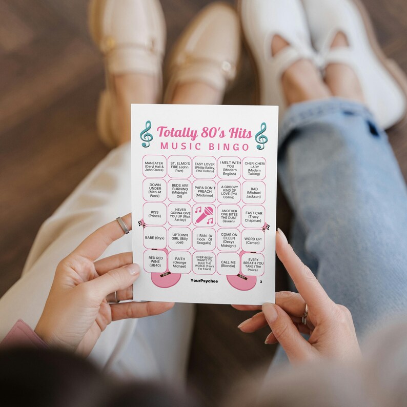Pu&ograve; includere: Una scheda di gioco rettangolare bianca intitolata Totally 80's Hits Music Bingo con note musicali color ottanio, un'icona di microfono rosa e illustrazioni di chitarre rosa. La griglia contiene venticinque riquadri con vari titoli di canzoni.