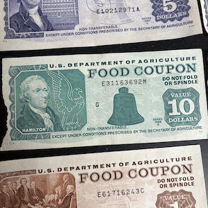 May include: Three vintage food coupons from the U.S. Department of Agriculture. The coupons are green, blue, and brown with the text "FOOD COUPON" and the value of the coupon printed on each. The coupons are non-transferable and are to be used only under conditions prescribed by the Secretary of Agriculture.