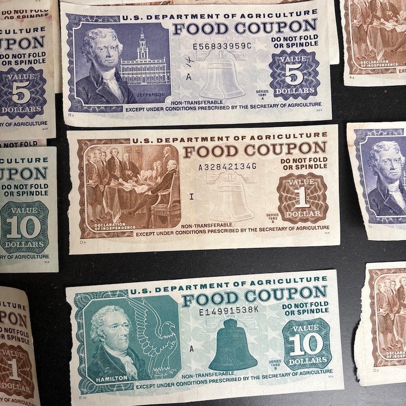 May include: A collection of vintage US Department of Agriculture food coupons. The coupons are printed on white paper with blue, green, and brown ink. The coupons feature images of historical figures, including Thomas Jefferson, Alexander Hamilton, and George Washington. The coupons are for various denominations, including &pound;1, &pound;5, and &pound;10.