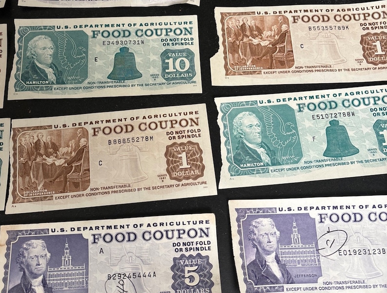 May include: A collection of vintage food coupons from the U.S. Department of Agriculture. The coupons are printed on paper and feature images of historical figures like Hamilton and Jefferson. The coupons have different values, including 1, 5, 10 dollars. The coupons have a bell design and the text "DO NOT FOLD OR SPINDLE".