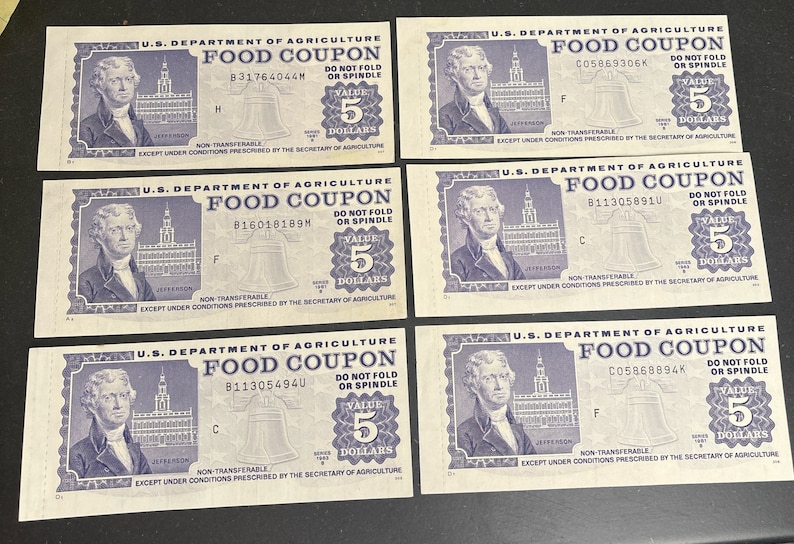 May include: Six vintage US Department of Agriculture food coupons, each worth 5 dollars. The coupons are printed on white paper with blue ink and feature a bell, a building, and a portrait of Thomas Jefferson. The coupons have a serial number and a date.